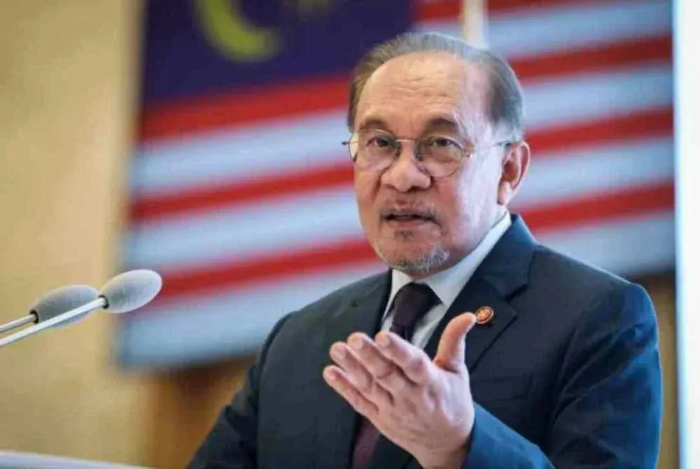 Anwar Ibrahim speaking in front of a Malaysian flag and microphones