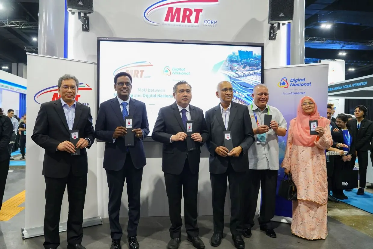 Six officials, including Transport Minister Anthony Loke, hold RTS Link Touch 'n Go cards in front of a screen showing the MRT Corp and Digital Nasional MoU