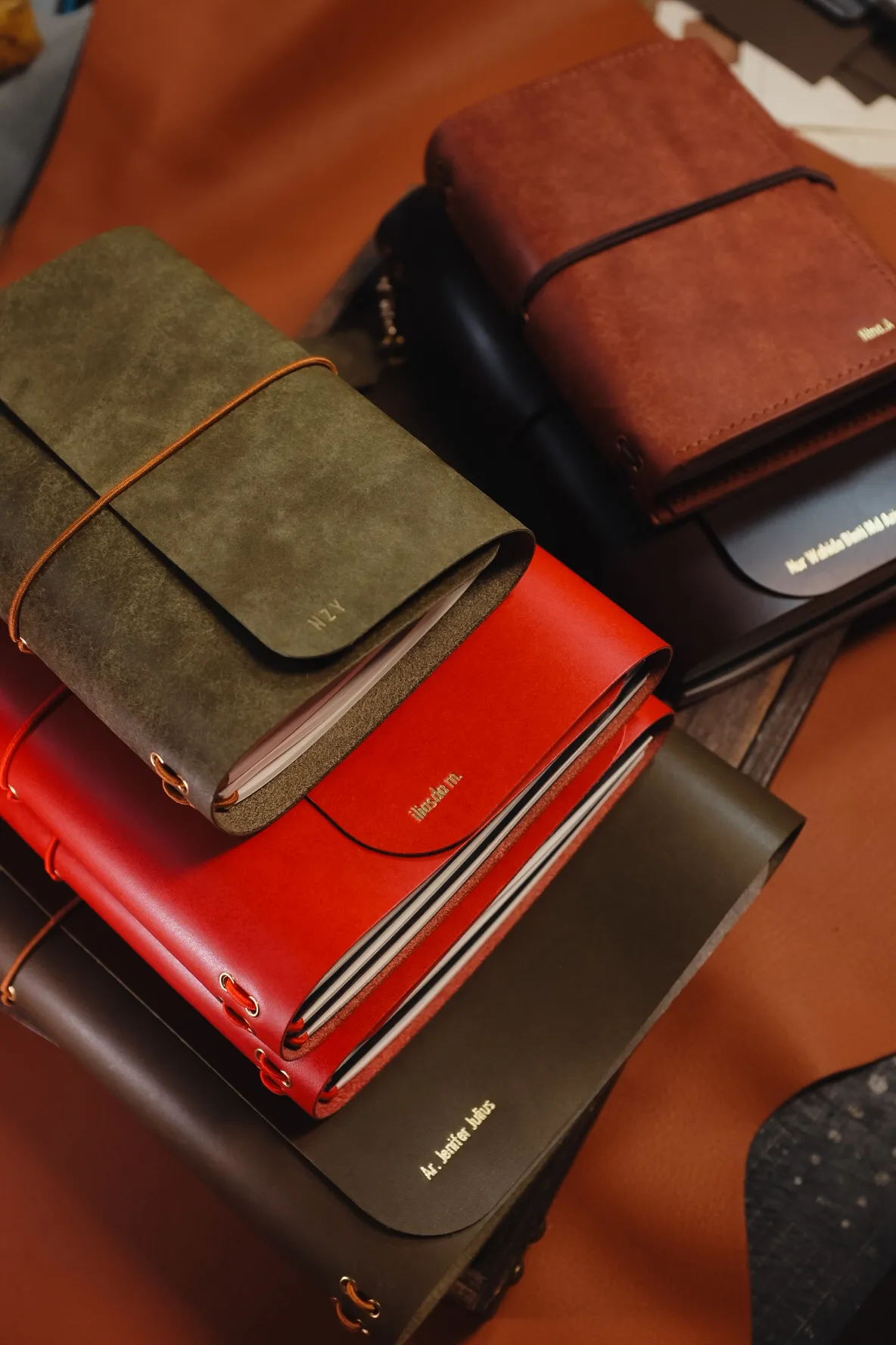 Timbunan jurnal kulit buatan tangan berwarna hijau zaitun, merah dan coklat dengan nama pelanggan dicetak emas