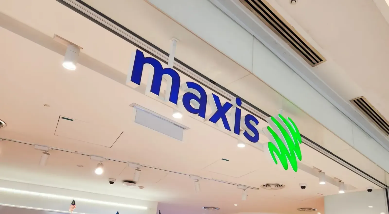 A Maxis sign with blue lettering and a green logo above a shop front