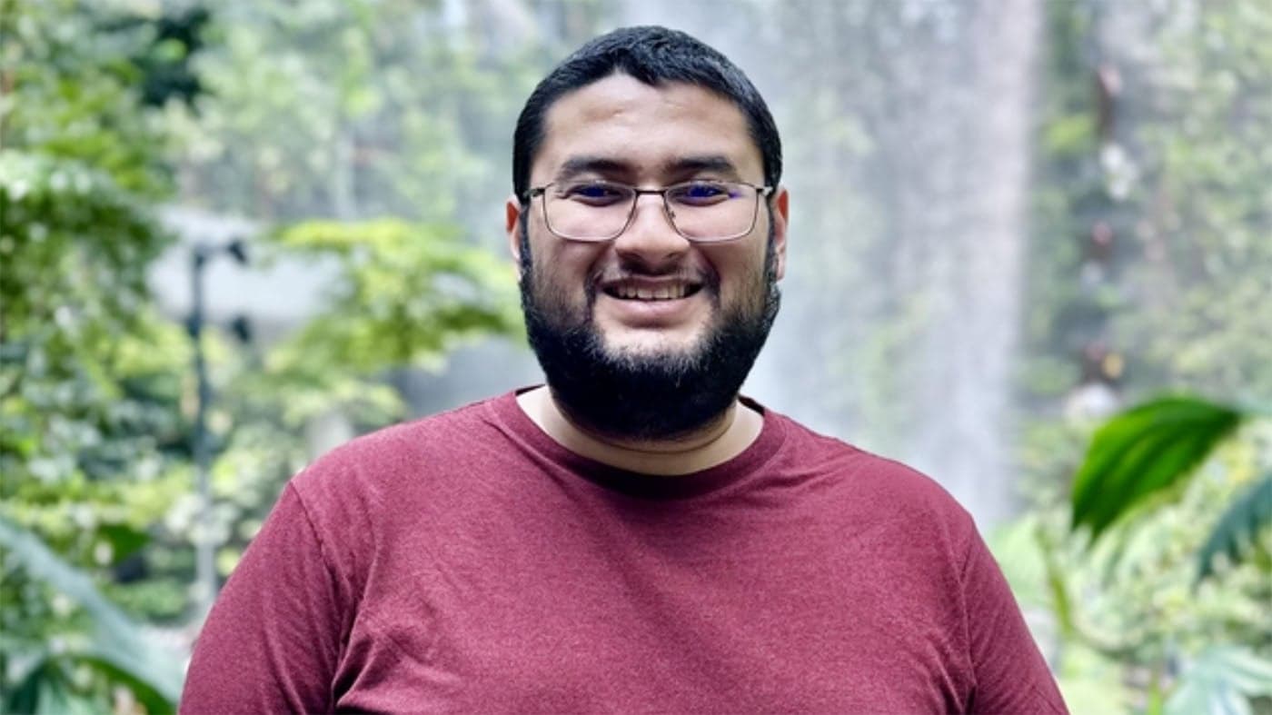 Mohammad Hasif Afiq tersenyum dengan latar air terjun dan pokok hijau