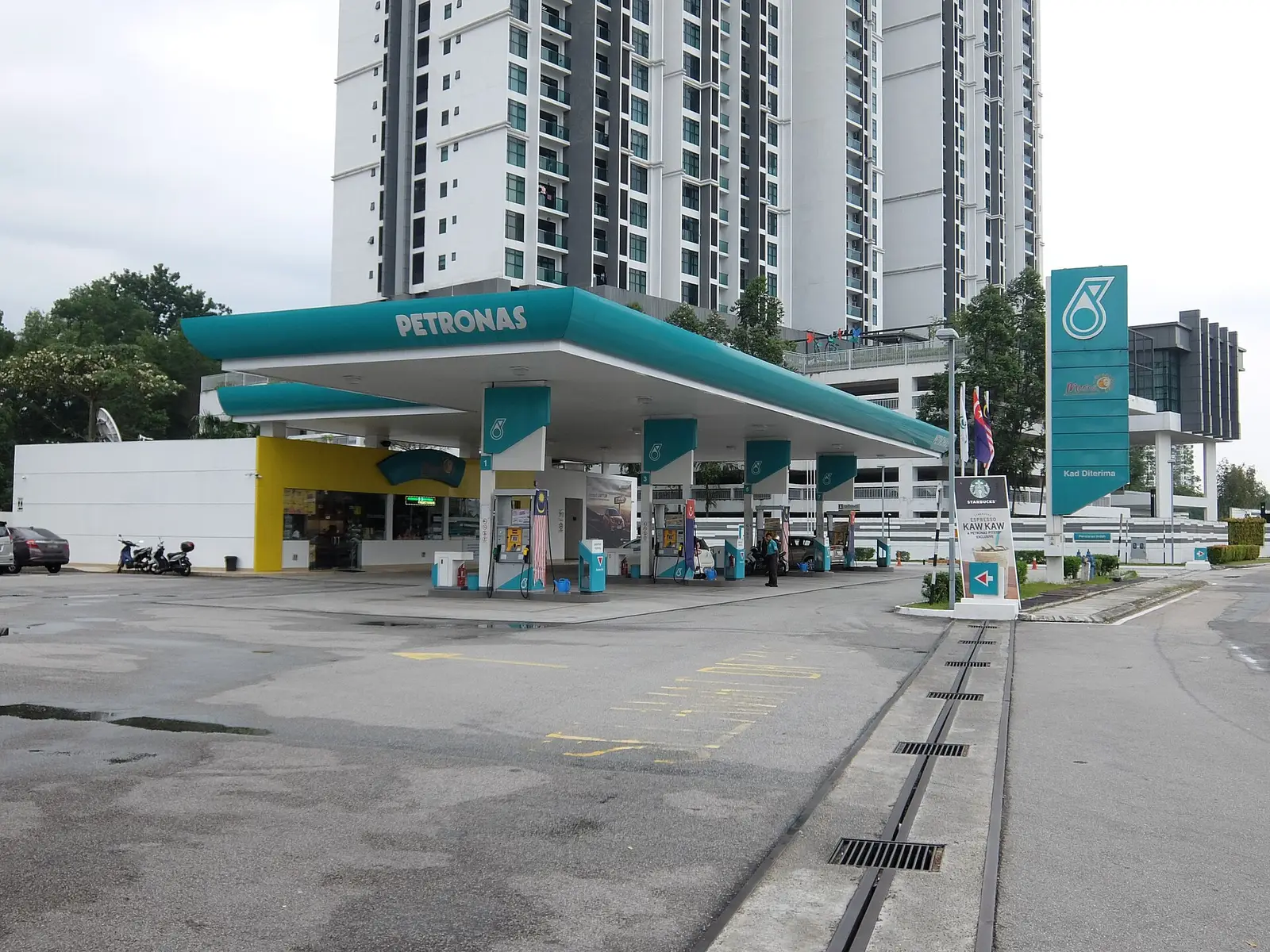 Stesen minyak Petronas di Persiaran Indah, dengan pam minyak di bawah bumbung hijau dan pangsapuri tinggi di belakang