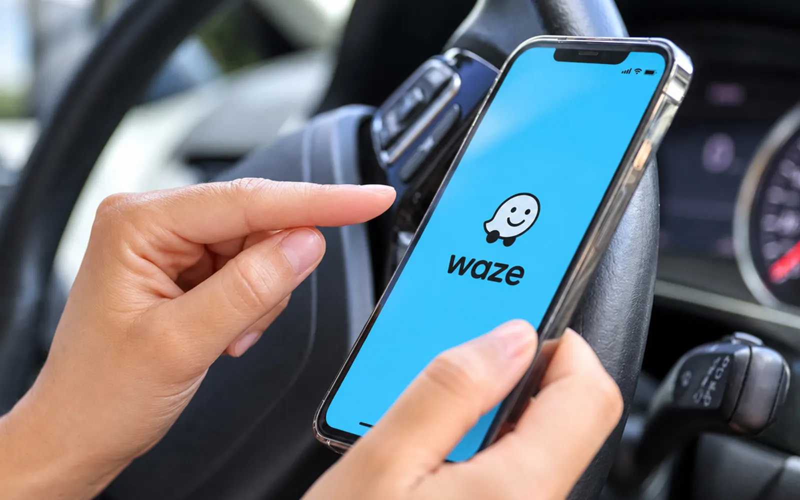 Dua tangan memegang telefon pintar yang memaparkan logo Waze di dalam kereta
