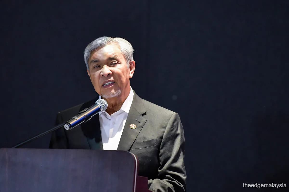 Datuk Seri Dr Ahmad Zahid Hamidi speaking at a lectern with a microphone, against a dark wall